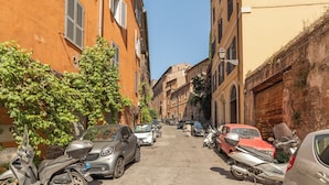 A narrow street lined with parked cars and scooters, buildings with shutters, and a clear blue sky. - Monti  Apartments (Rome)