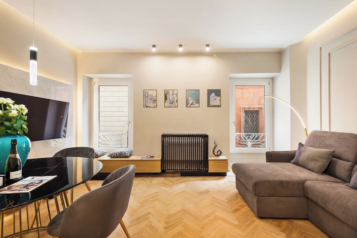 A modern living room with a sectional sofa, a dining table with chairs, a TV, and artwork on the wall.