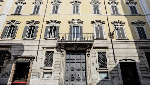 Fachada de edificio con entrada central, varios ventanales con contraventanas y un balcón decorativo.