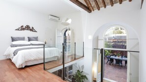 Un dormitorio con cama, barandilla de vidrio y vista a un patio exterior.