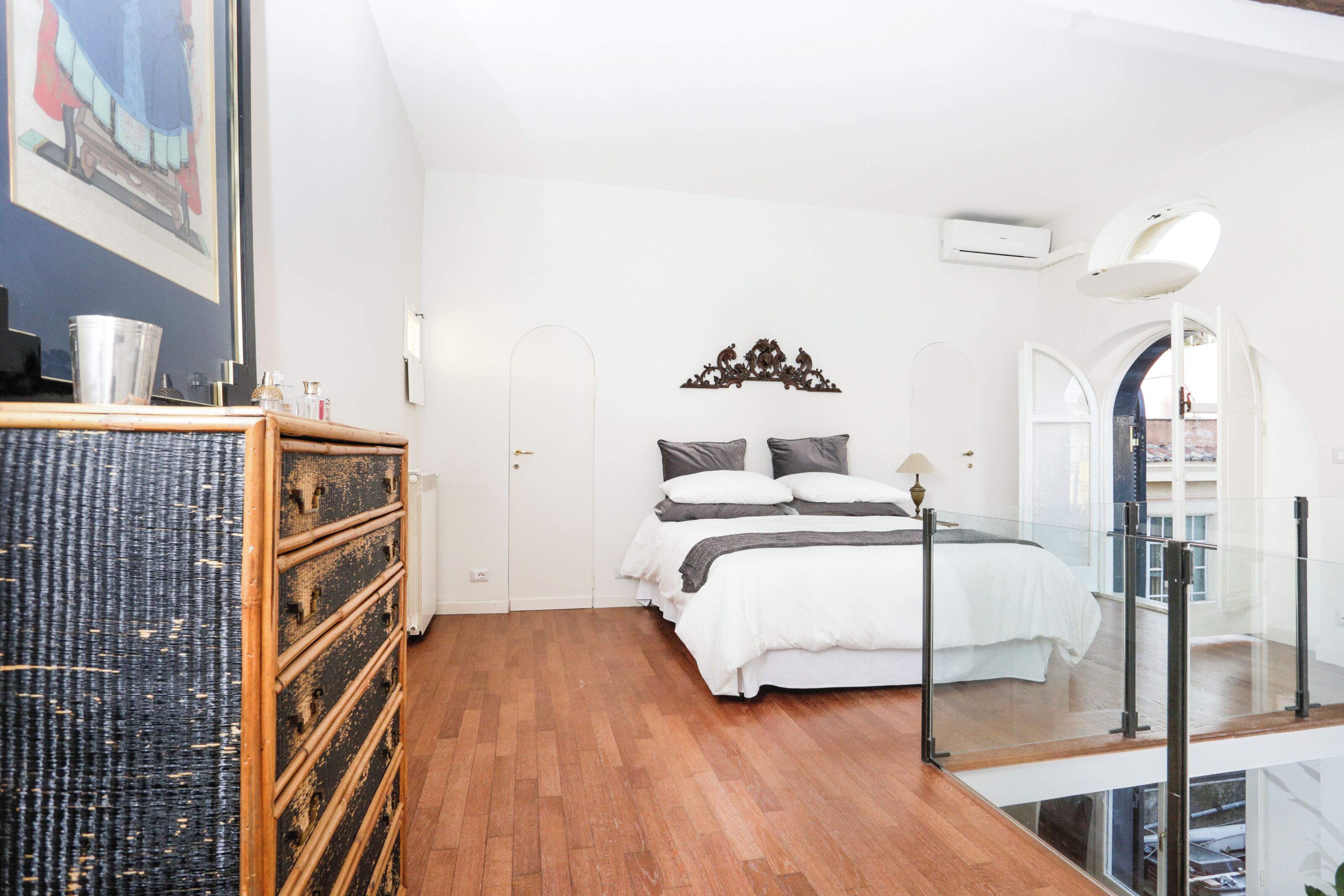 Une chambre avec un plancher en bois, un lit avec une literie blanche, une commode et un tableau accroché au mur.