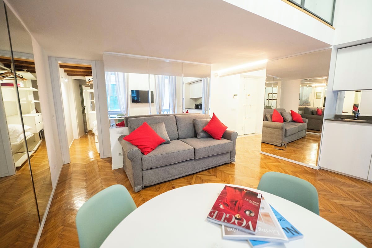 A modern living room with a grey sofa, red cushions, and a white table with magazines.