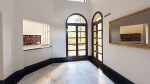 Un pasillo con suelo de mármol, dos puertas arqueadas, un ventanal y un espejo en la pared.