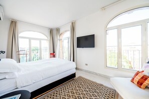 Une chambre d’hôtel avec un lit, une télévision, un canapé et de grandes fenêtres.