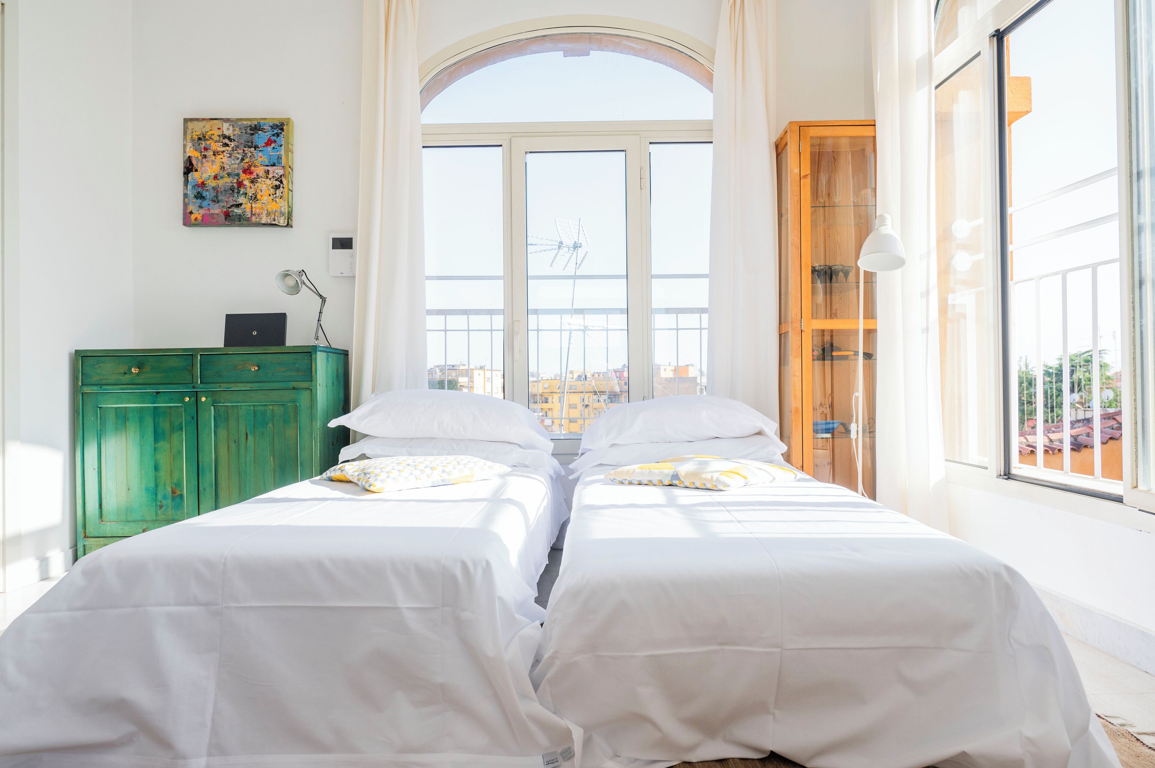 A room with two beds, a green cabinet, a painting, and a large window with a view.
