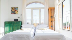 Una habitación con dos camas, un armario verde, un cuadro y un ventanal con vistas.