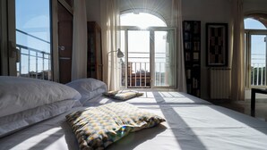 Un dormitorio con una cama grande, una ventana con cortinas, una estantería y vistas al exterior.