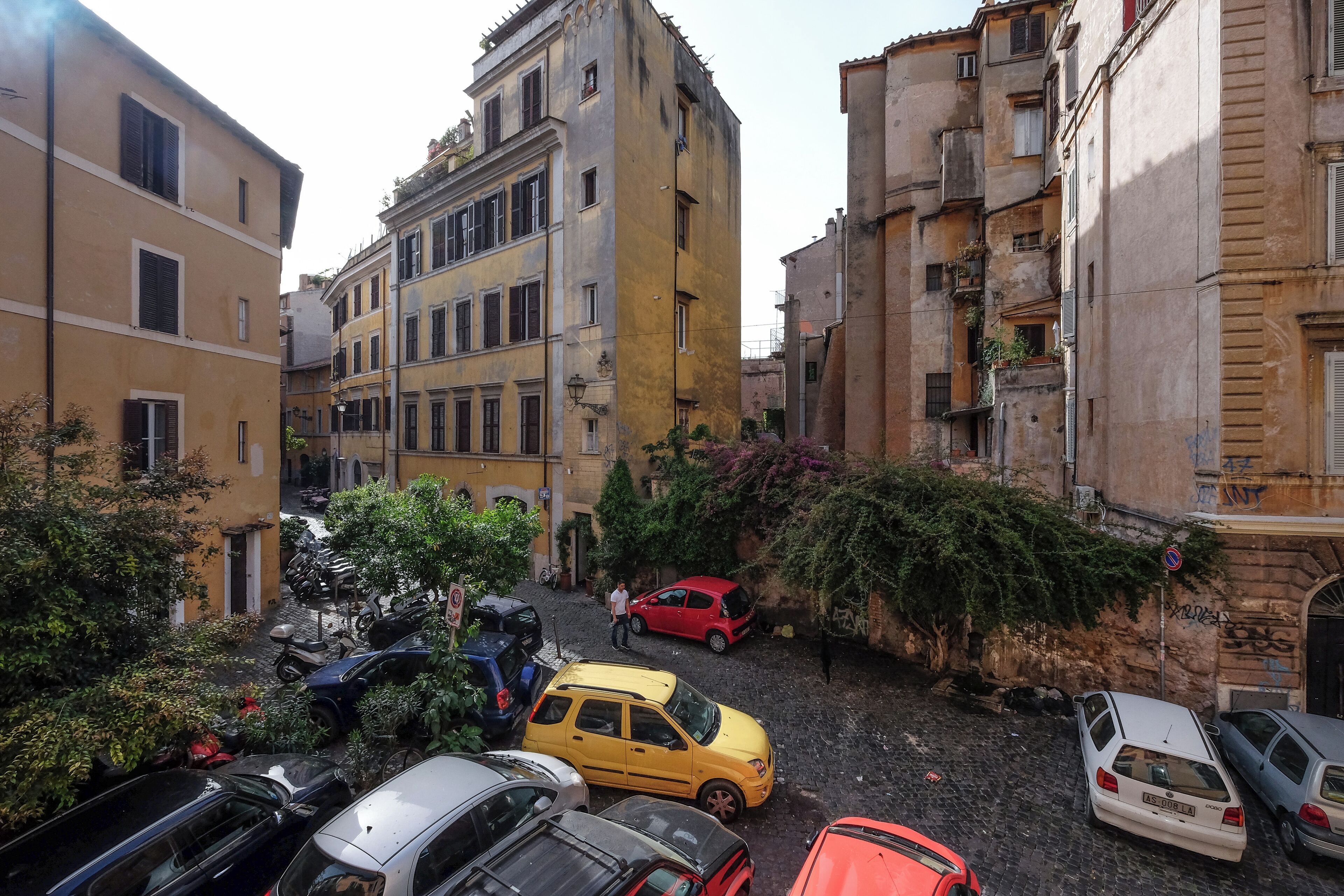 A narrow street with parked cars and buildings.
