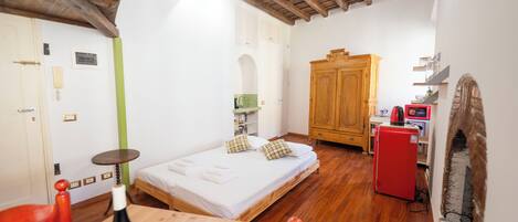 Un dormitorio con una cama de madera, una mesita con una botella, un refrigerador rojo y un armario de madera.