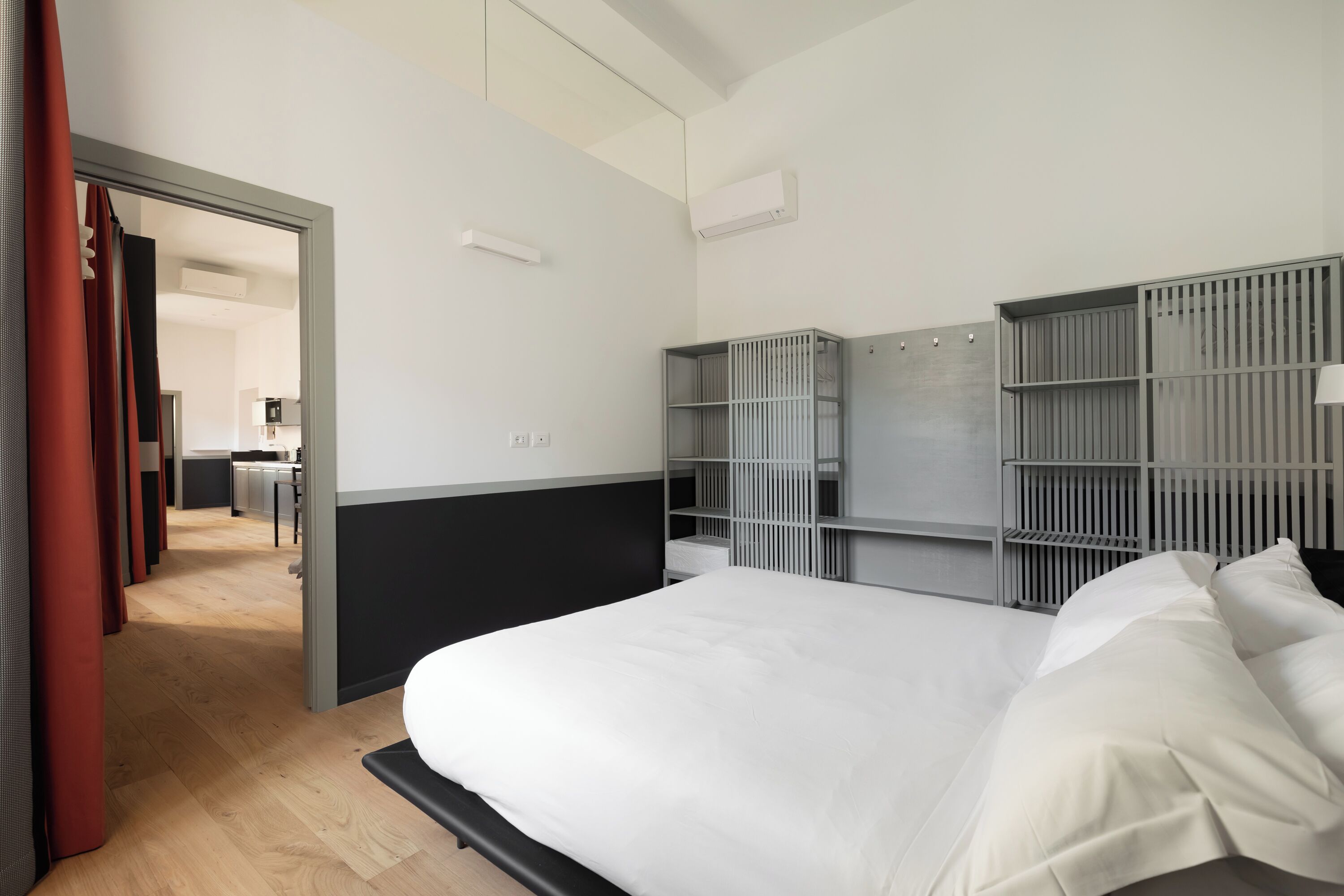 Ett modernt hotellrum med en stor säng, inbyggda förvaringsmöbler och utsikt över köksdelen.