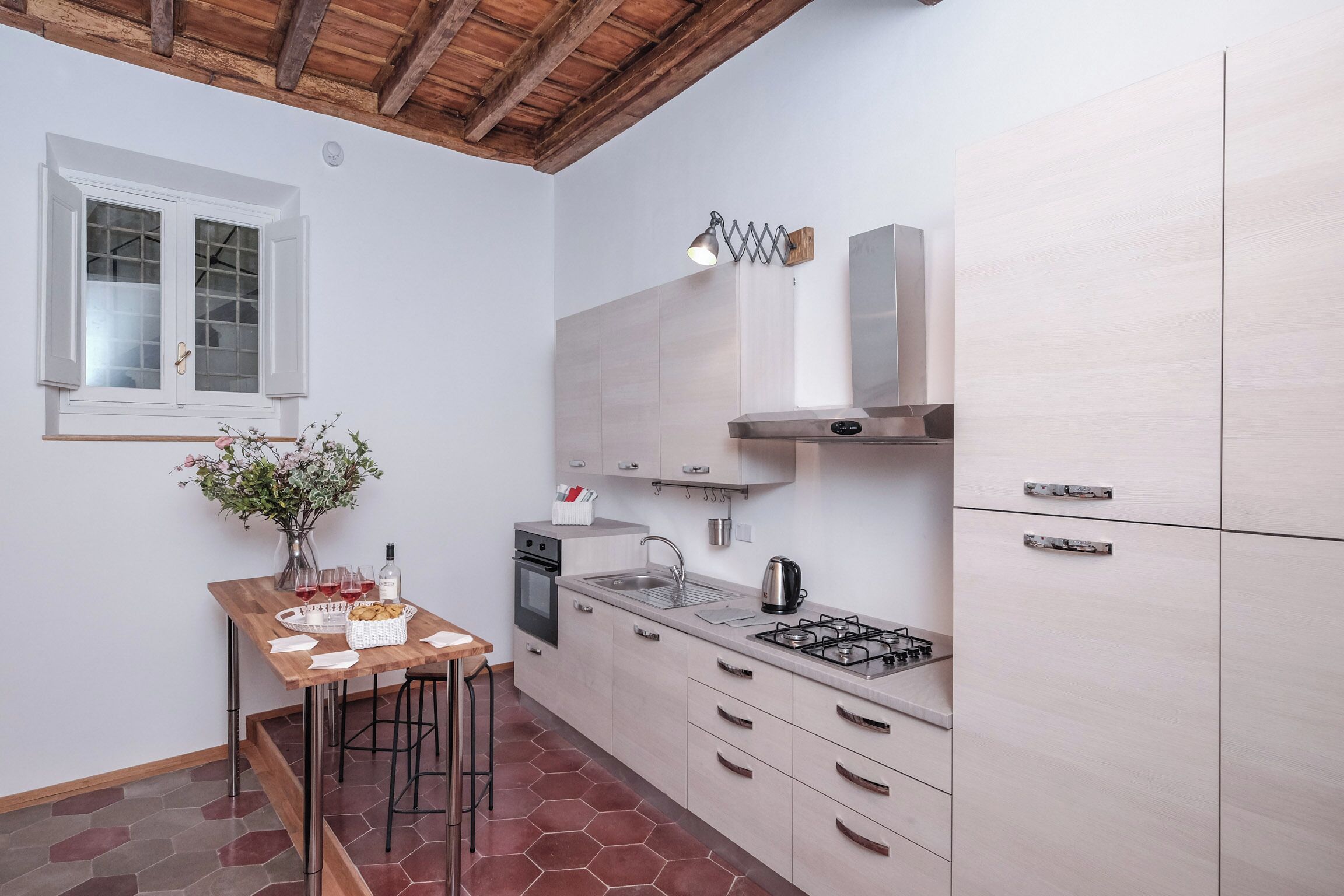 Una cocina compacta con una mesa de madera, taburetes de bar, horno empotrado, estufa a gas y armarios de colores claros.