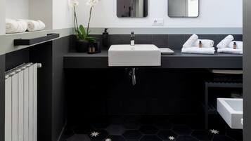 A modern bathroom with a black and white color scheme, featuring two sinks, a large mirror, and a black hexagonal tiled floor.