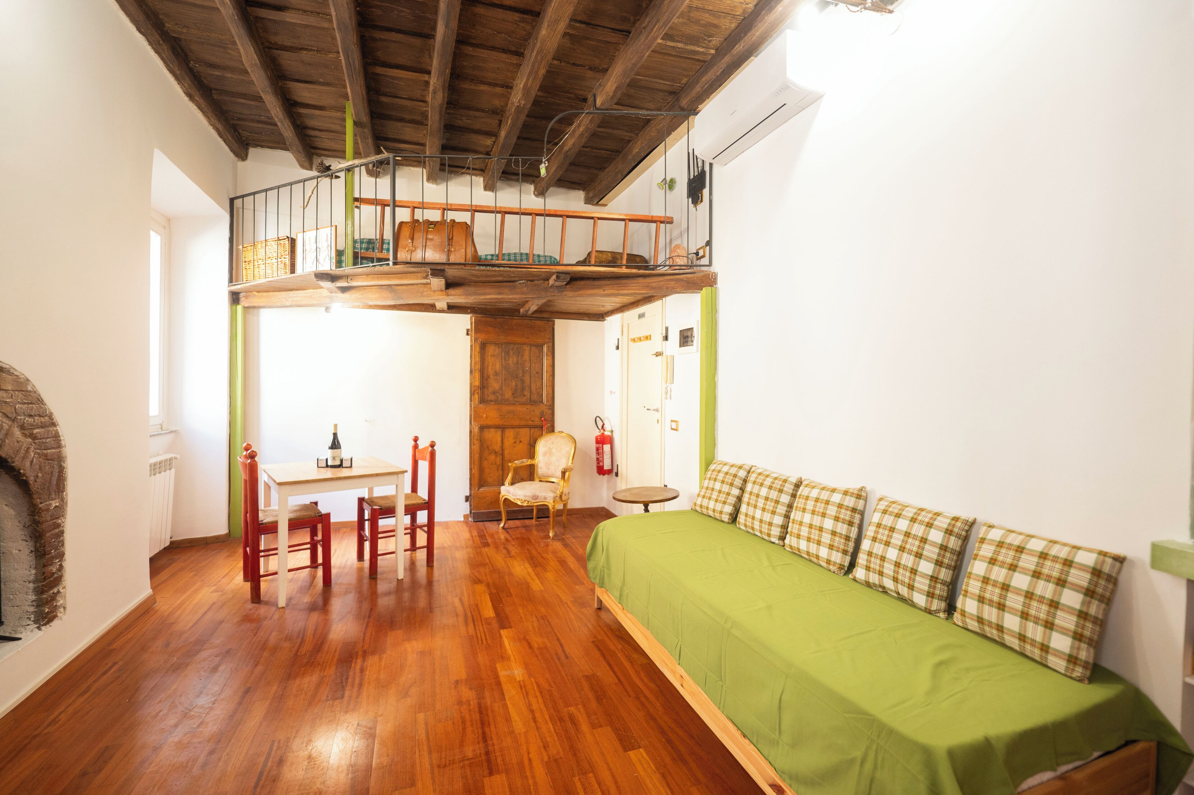 Een kamer met een hoogslaper, een eettafel met stoelen, een groene bank en een open haard.