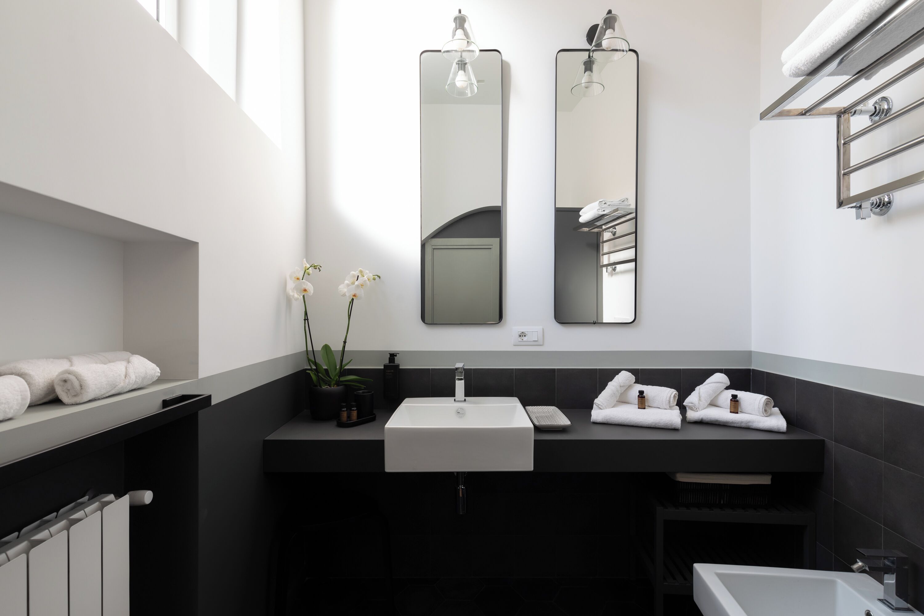 A modern bathroom with a large sink, two mirrors, a bathtub, and a towel rack.