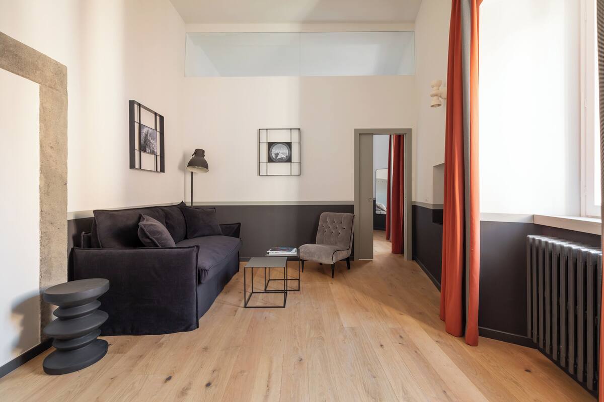 A modern living room with a sofa, armchair, and coffee table, a radiator, and a framed picture on the wall.