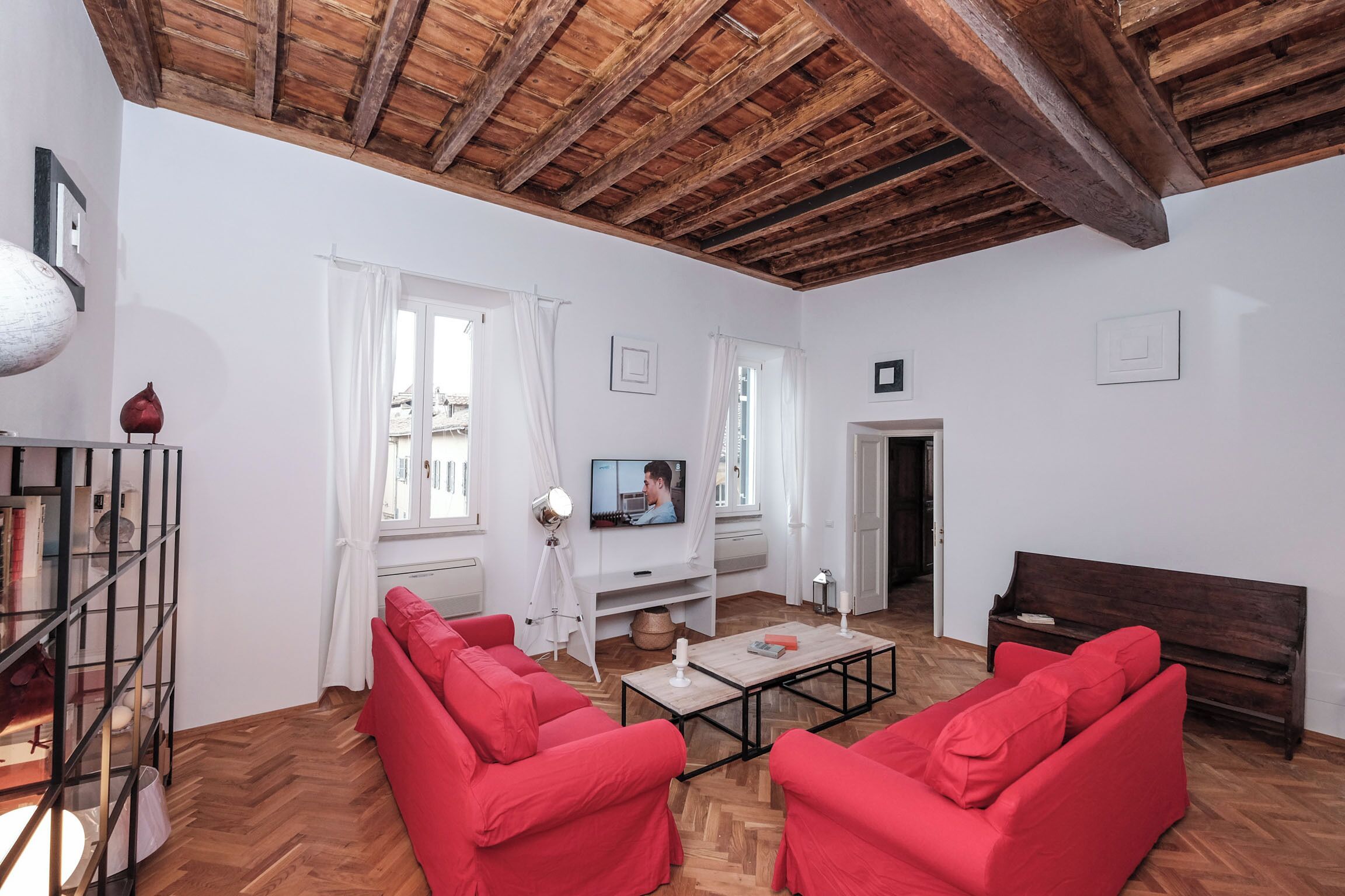 Una sala de estar con techo de madera, sofás rojos, una mesa de centro y un televisor sobre un mueble blanco.