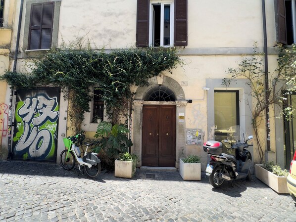 A building with a cobblestone street, a wooden door, and a motorcycle parked in front. - Trastevere Apartments (Rome)