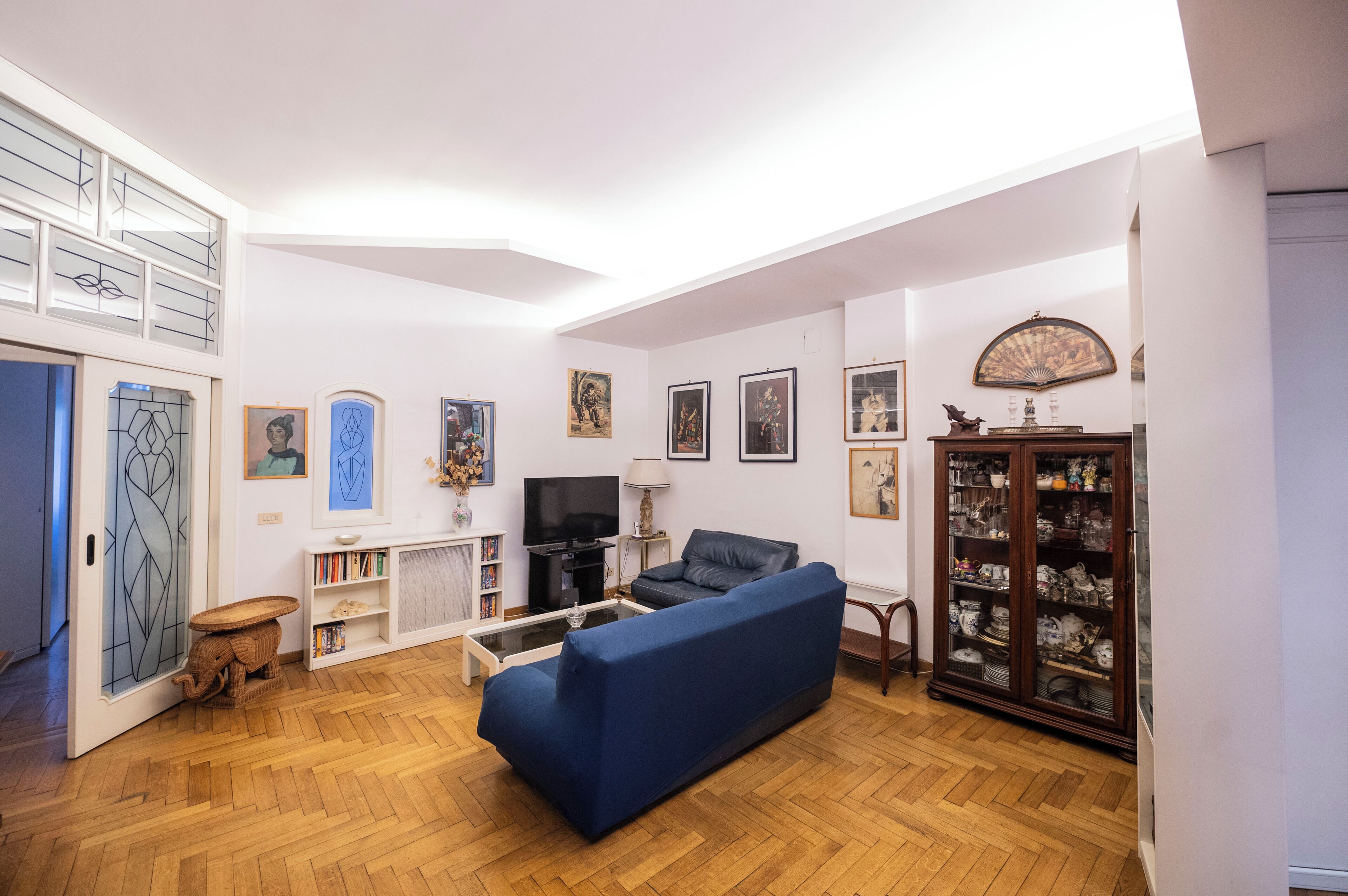 A living room with a blue sofa, a television, a bookshelf, and a decorative cabinet.
