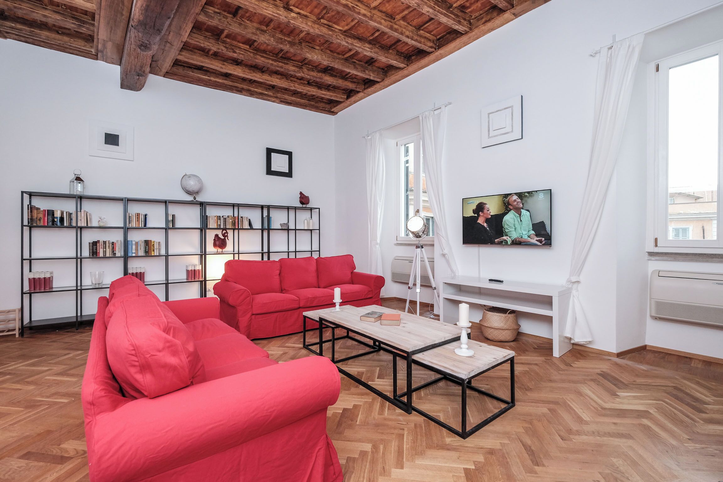 Uma sala de estar com um sofá vermelho, uma mesa de centro de madeira, uma estante e uma televisão.