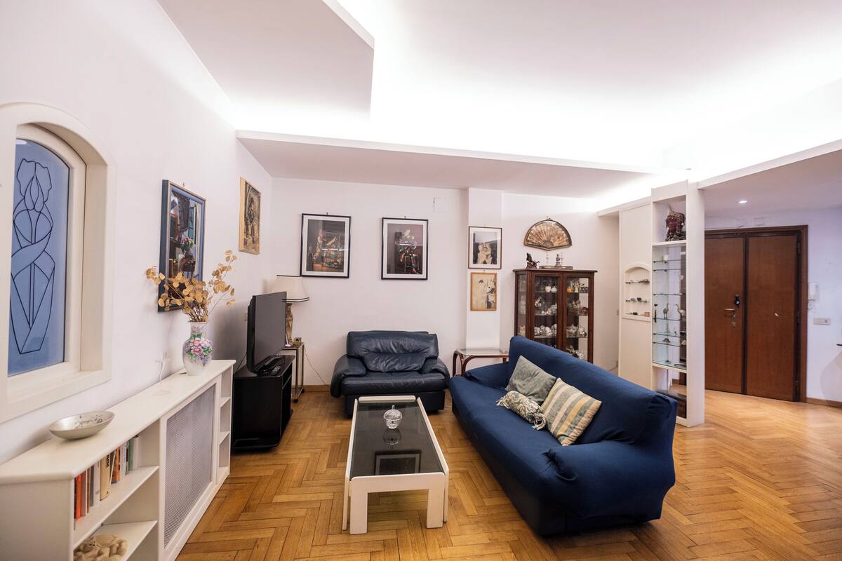 A living room with a blue sofa, a coffee table, a black leather chair, and a bookshelf.