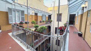 Ein Innenhof mit überdachtem Gang, Blumentöpfen und einem Gebäude mit Kruzifix an der Fassade.