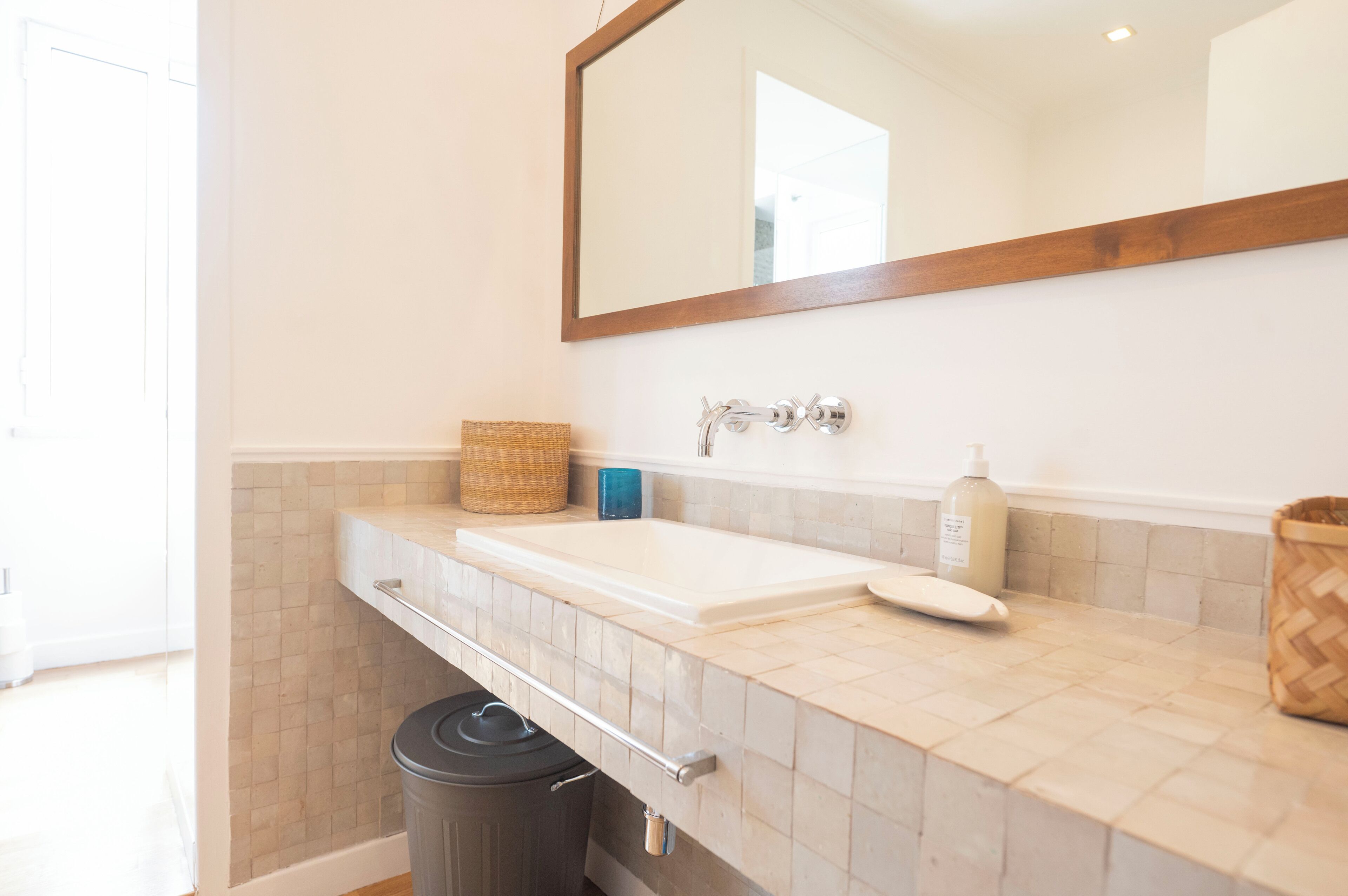 A bathroom with a white sink, a mirror, and a trash can.