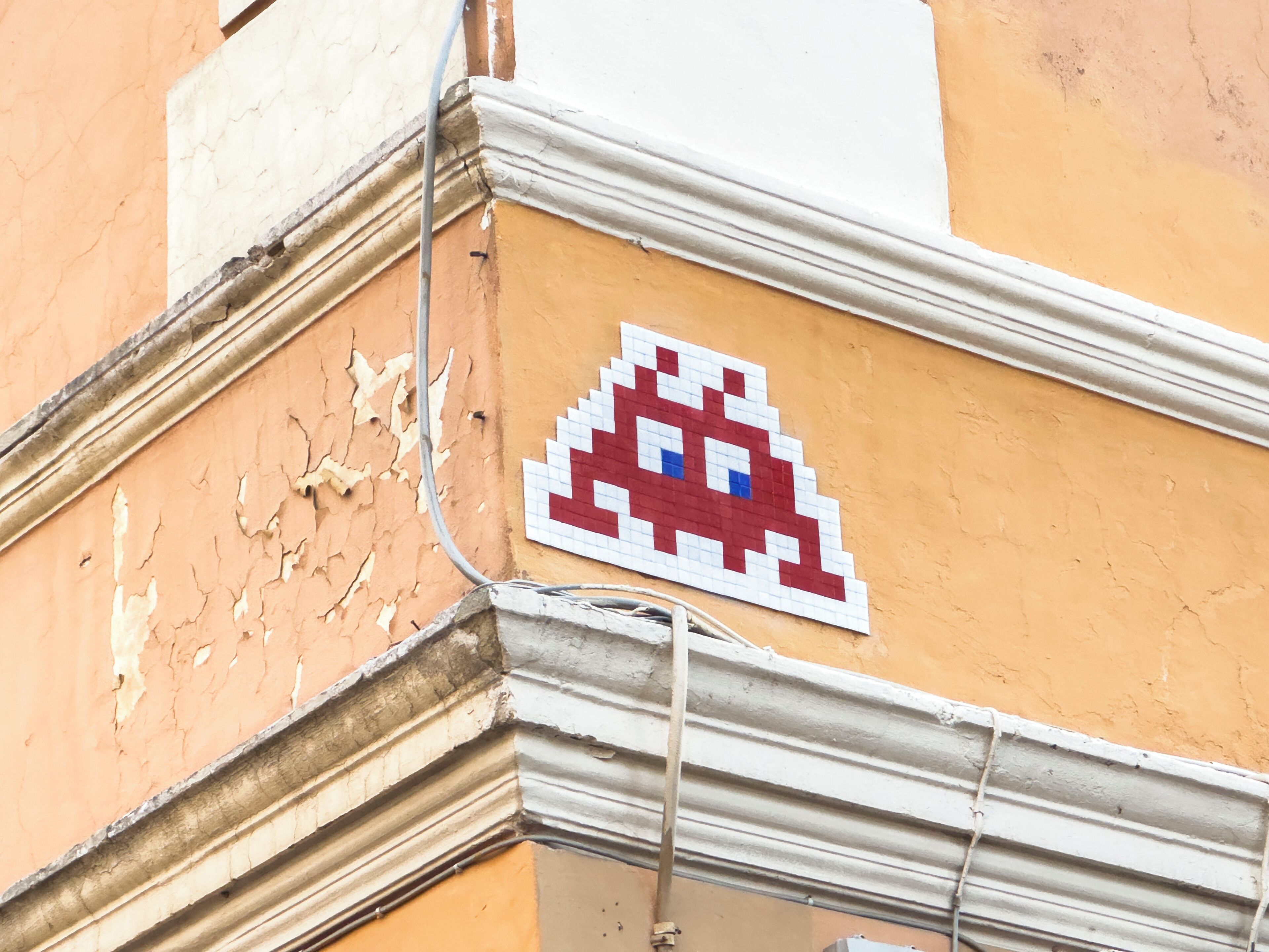 Esquina de un edificio con pintura descascarada y un letrero de un extraterrestre pixelado.
