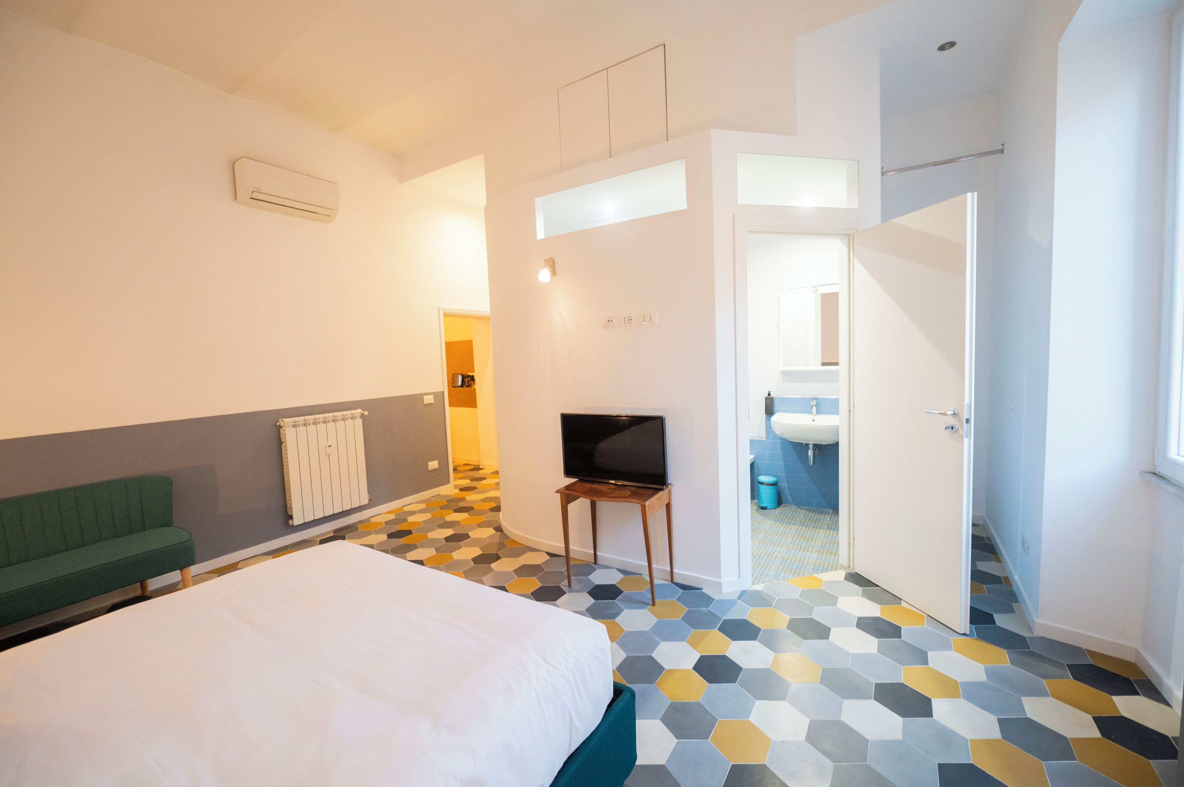 A hotel room with a bed, a green sofa, a television on a small table, and a bathroom visible through an open door.