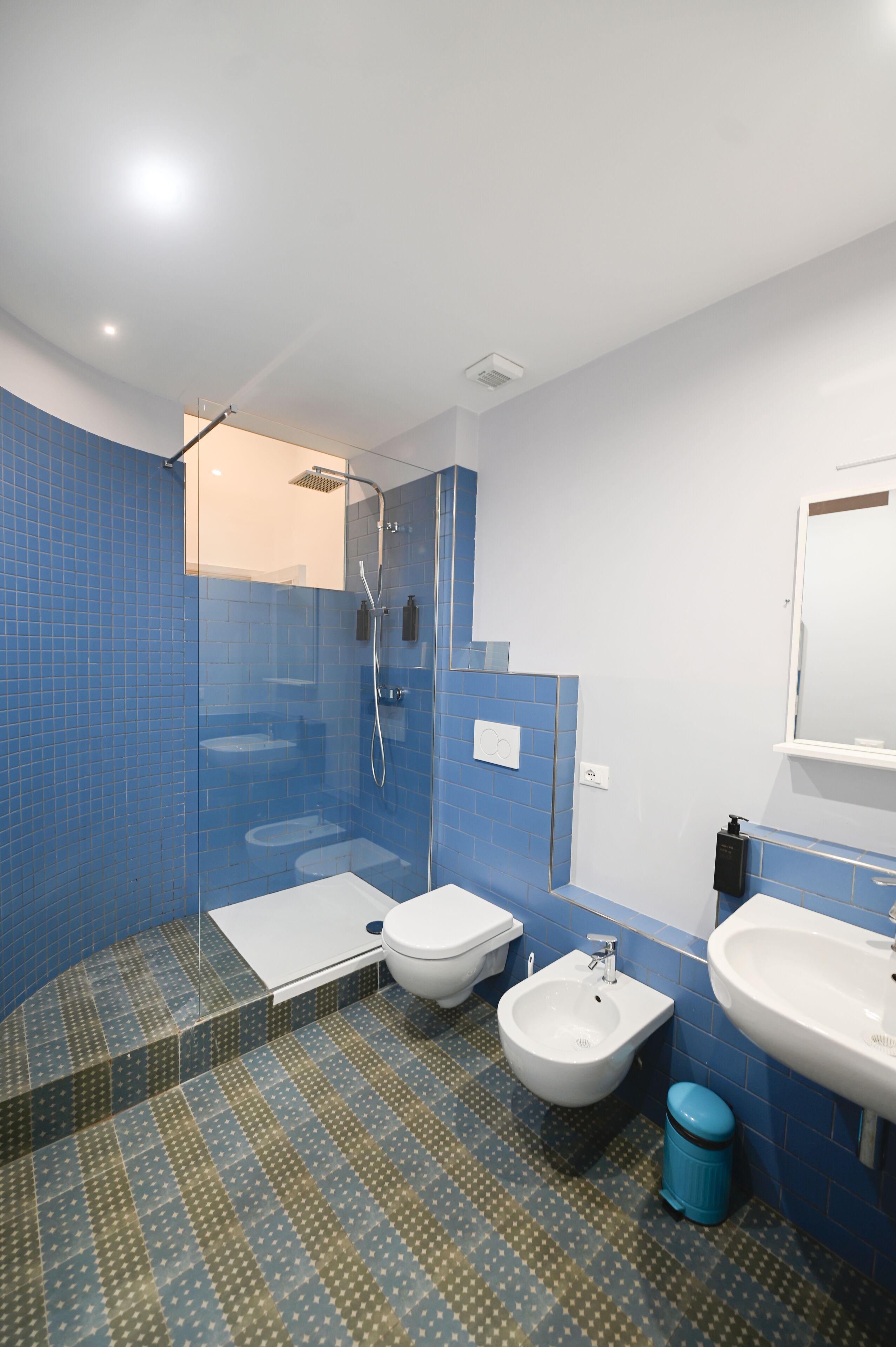 A modern bathroom with blue tiled walls, a shower, a bidet, a toilet, and a sink.