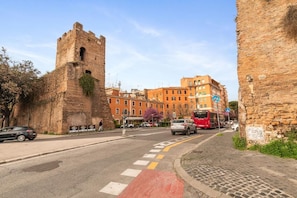 A street with a historic stone tower, modern buildings, and a red bus. - Termini Station Lightsome 3Br Apartment  (Rome)