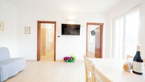 A bright living room with a sofa, a dining table with chairs, a TV mounted on the wall, and a small plant on the floor. - Terraced Apartments By The Ancient Appian Way  (Rome)