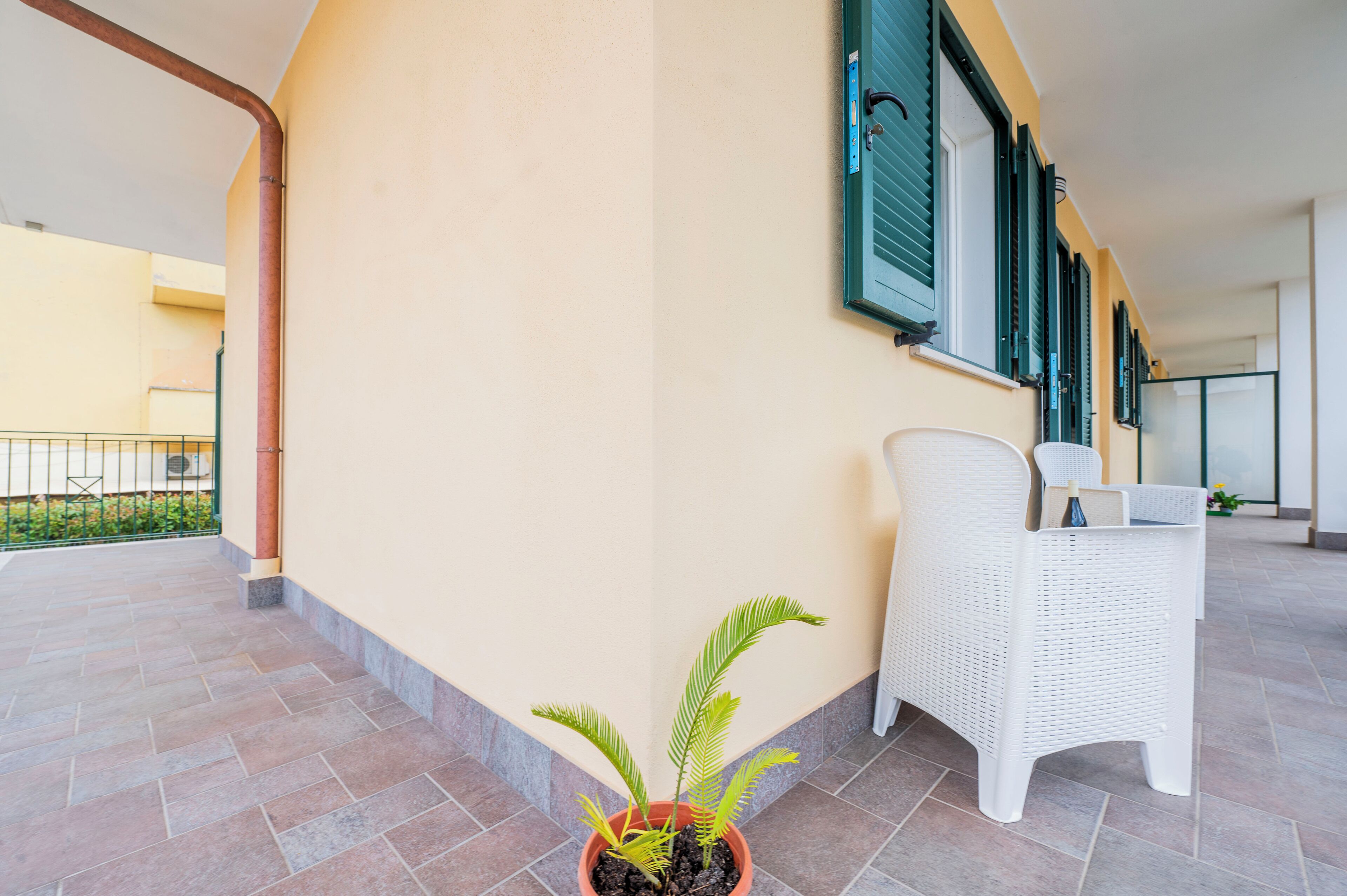 A clean, tiled balcony with a potted plant and a white wicker chair.