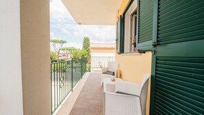 A balcony with a white wicker sofa, a small table with a bottle, and a green shuttered window. - Terraced Apartments By The Ancient Appian Way  (Rome)