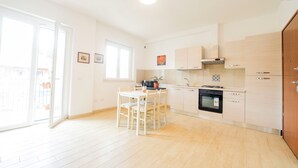 A modern kitchen with white cabinets, a built-in oven, and a dining area with a table and chairs. - Terraced Apartments By The Ancient Appian Way  (Rome)