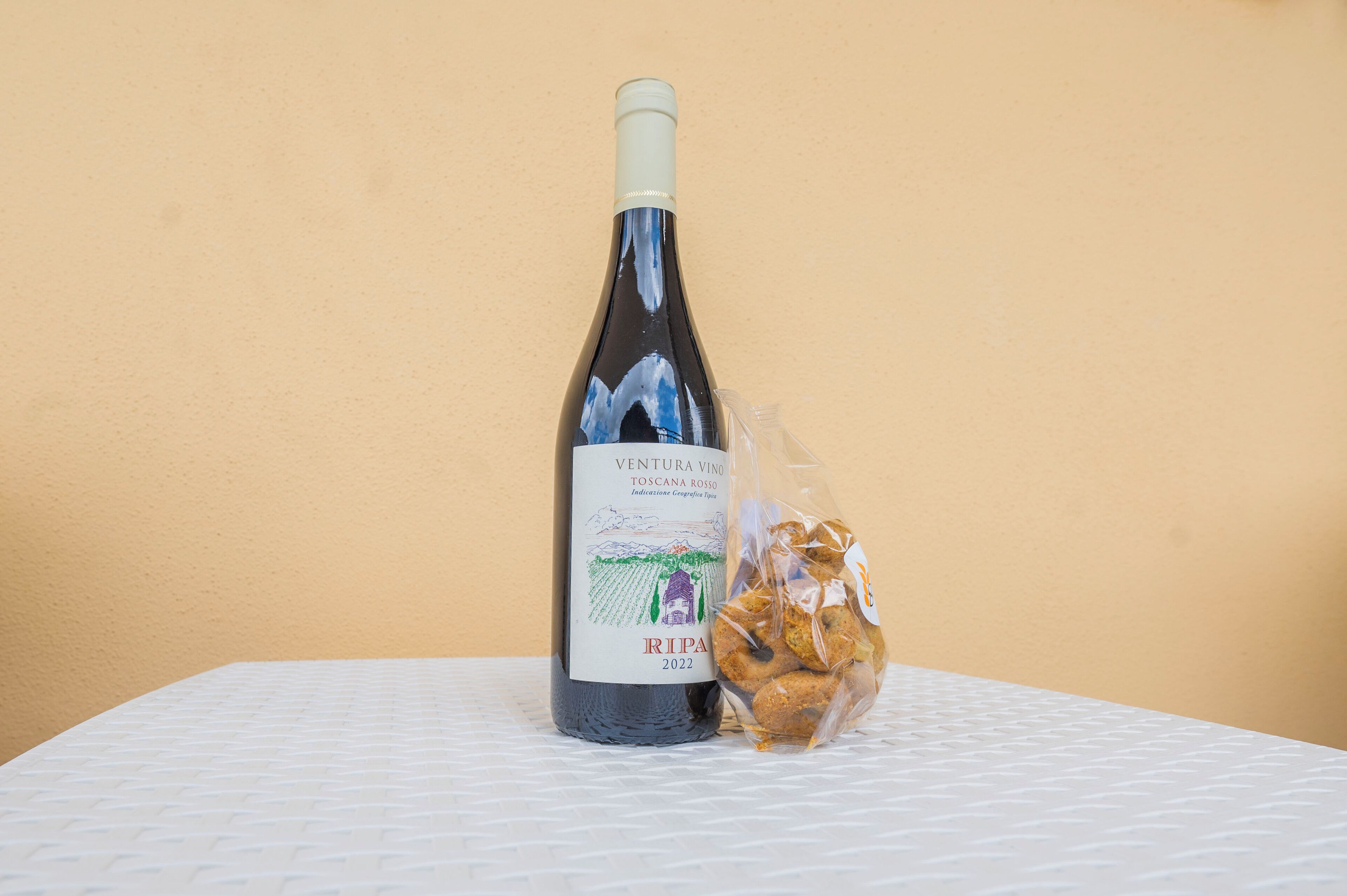 A bottle of wine and a bag of cookies on a table against a plain wall.