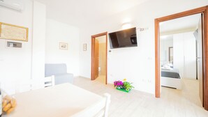 A bright, modern room with a flat-screen TV mounted on the wall, a dining table with chairs, and a bed with a wooden headboard. - Terraced Apartments By The Ancient Appian Way  (Rome)