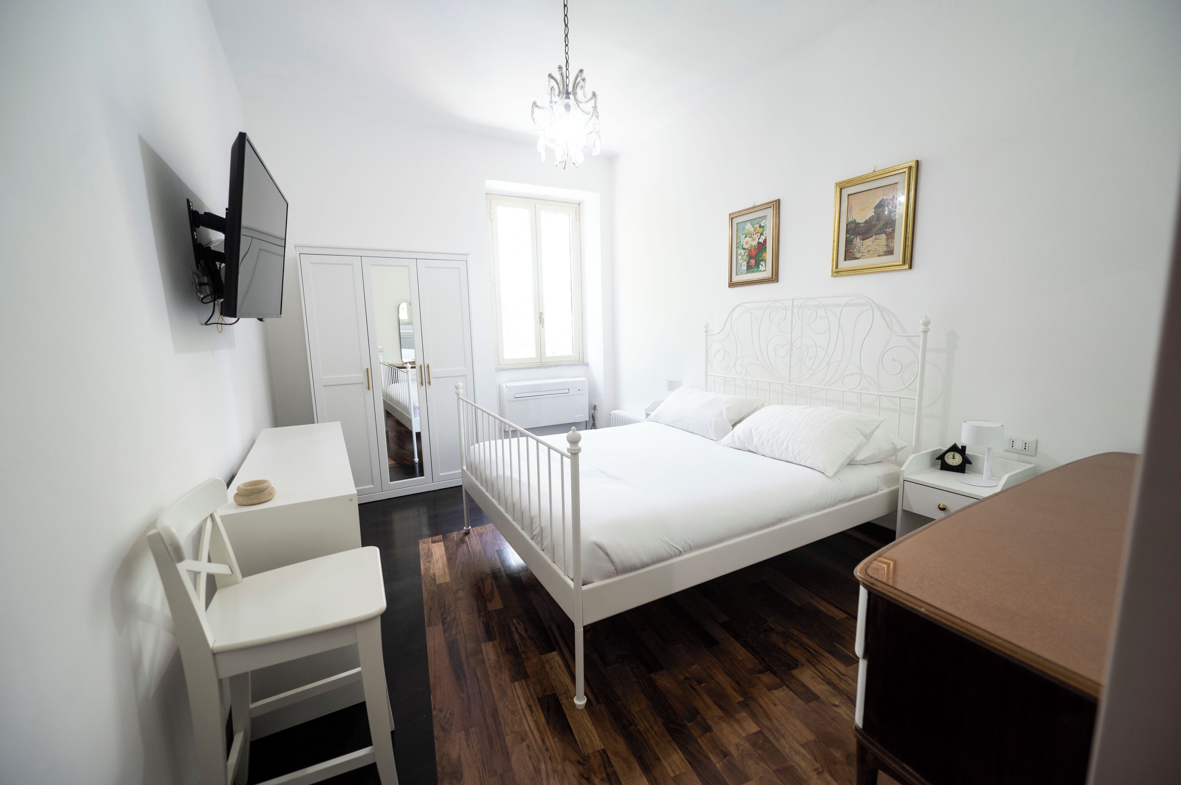 A bedroom with a bed, bedside table, chair, and a TV mounted on the wall.