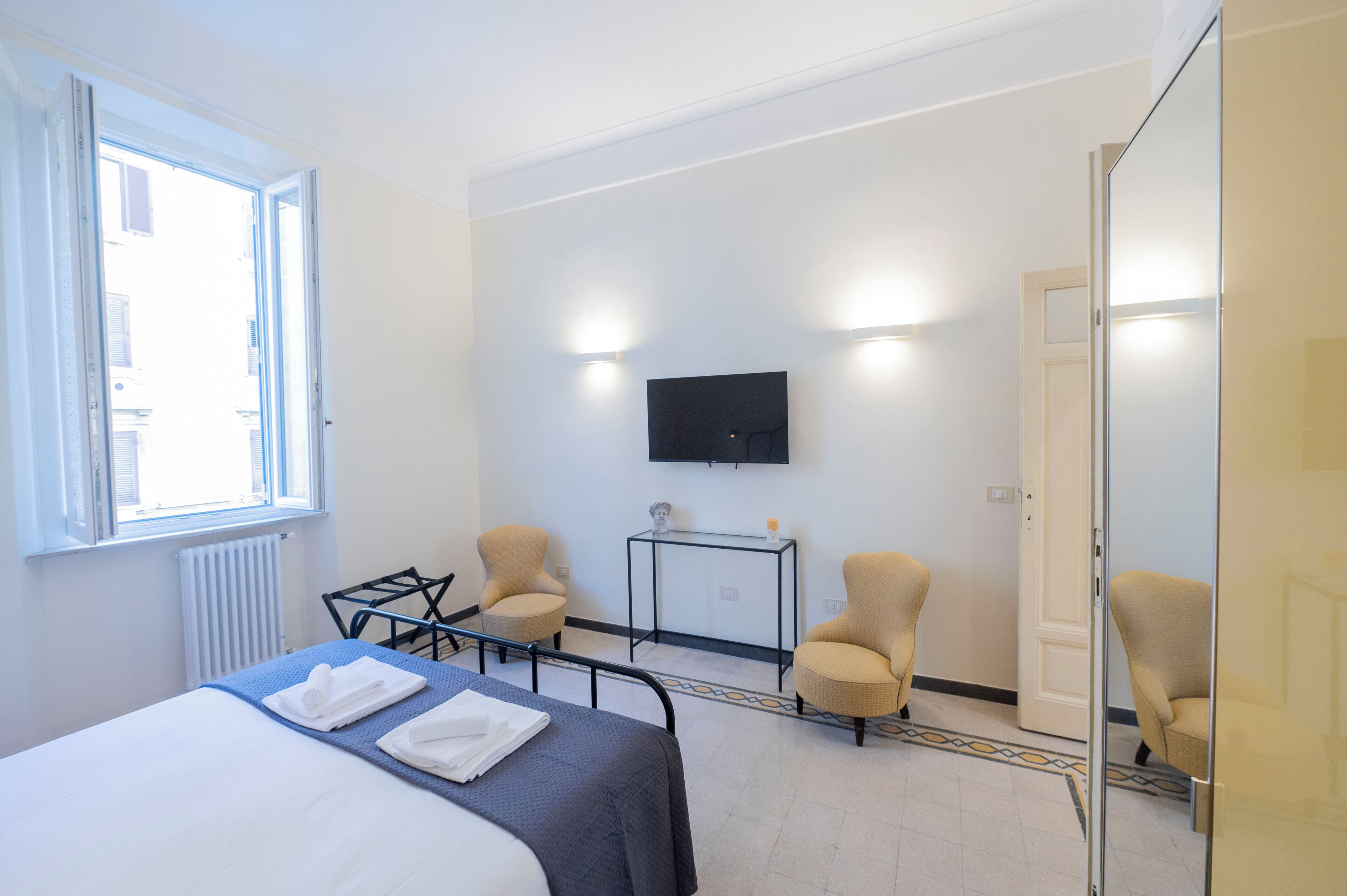 A hotel room with a bed, two armchairs, a small table, a television, and a window with blinds.