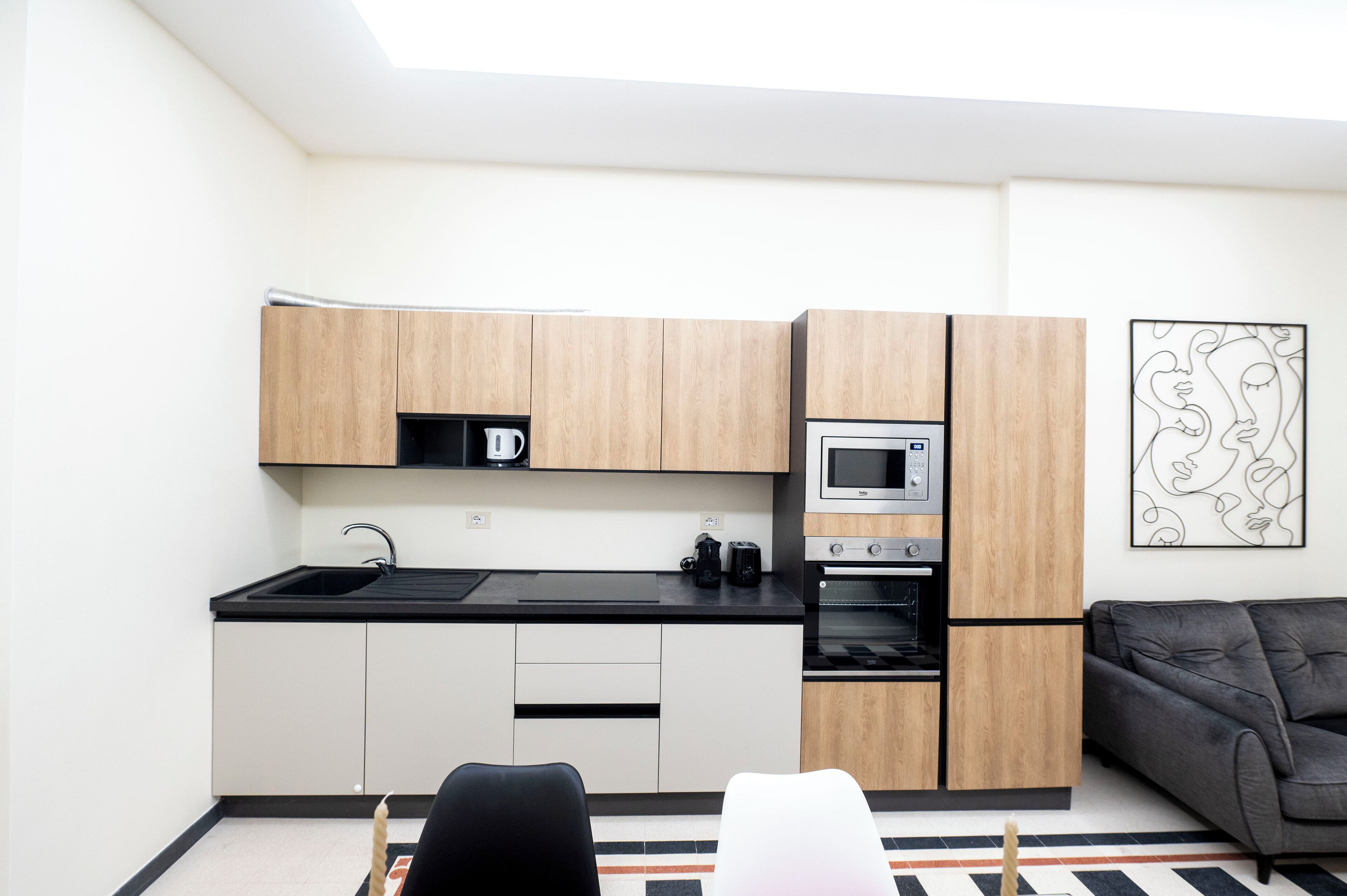 A compact kitchen with wooden cabinets, a microwave, and an oven. There is a black countertop and a black chair in the foreground.
