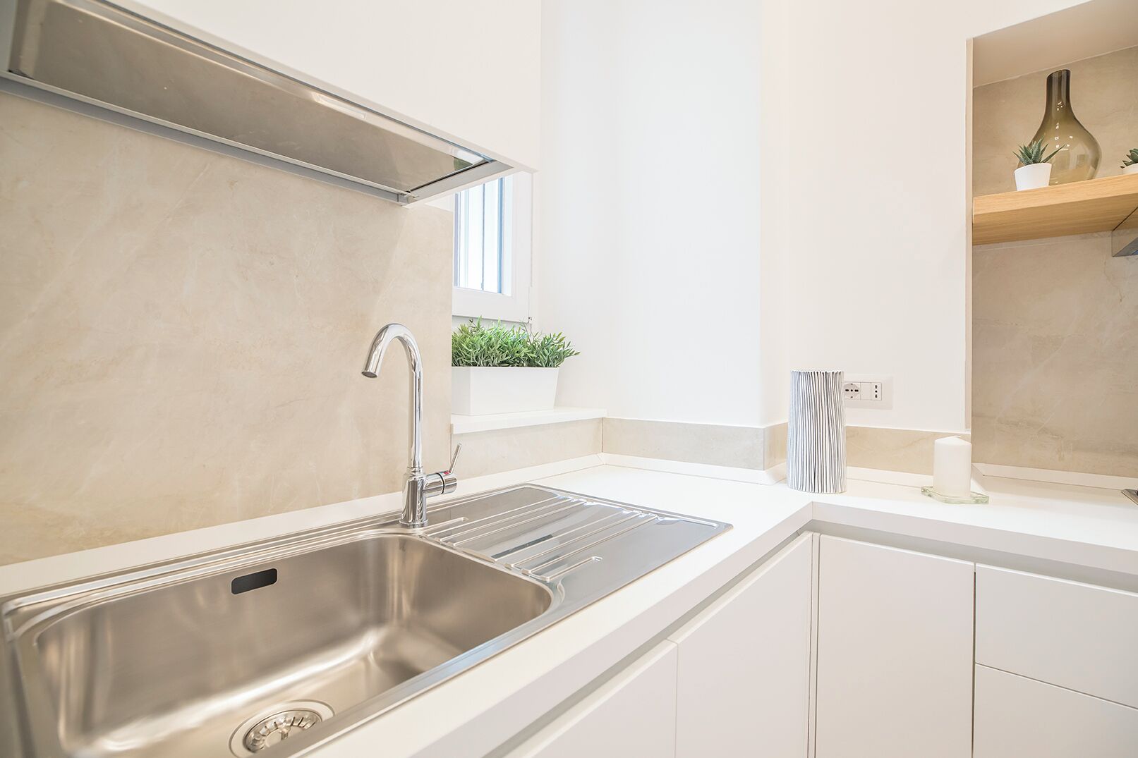 Una cocina moderna con un lavamanos de acero inoxidable, armarios blancos y un ventanal sobre el lavamanos.