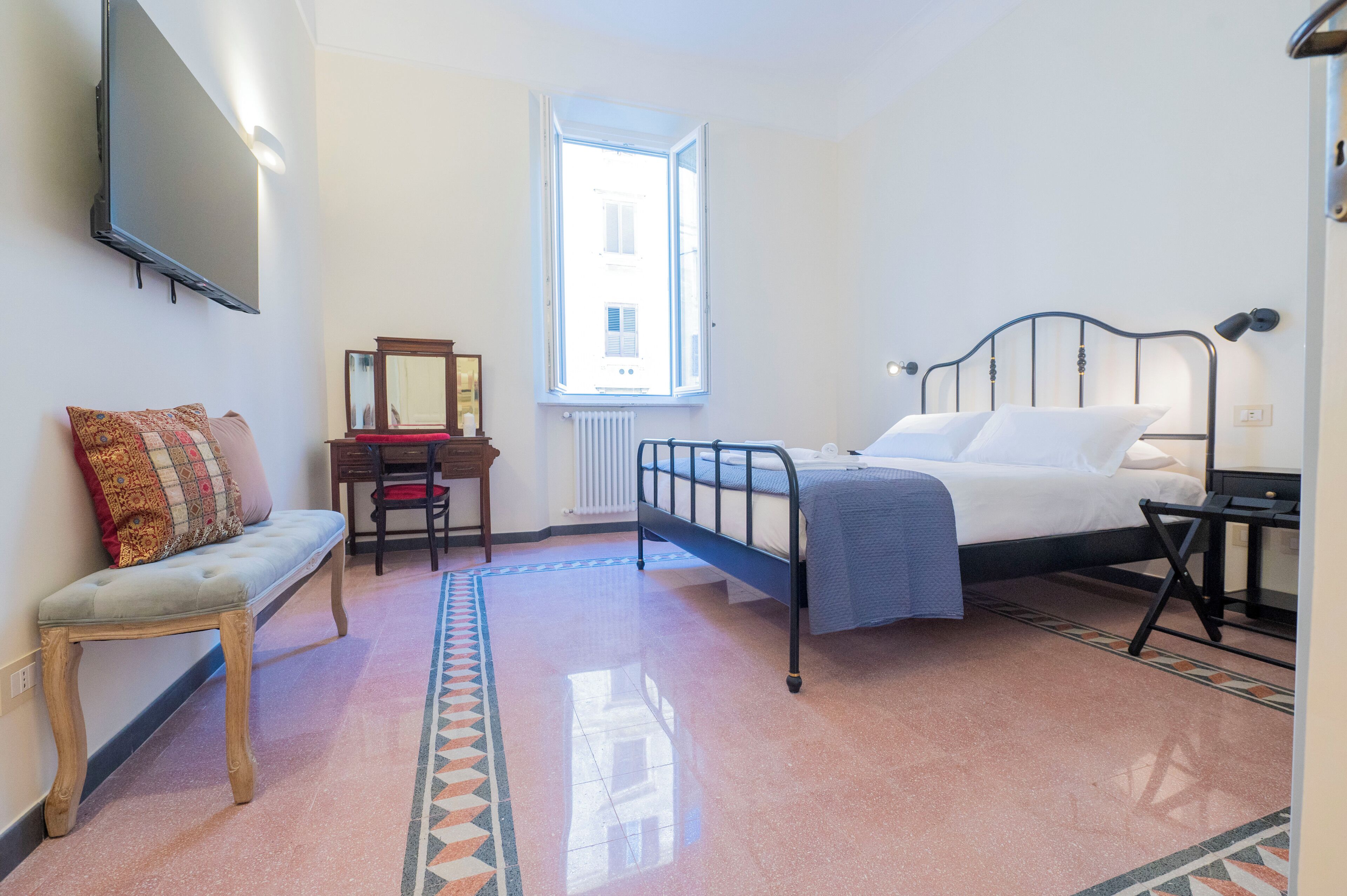 A bedroom with a bed, a bench, a desk, a mirror, and a window.