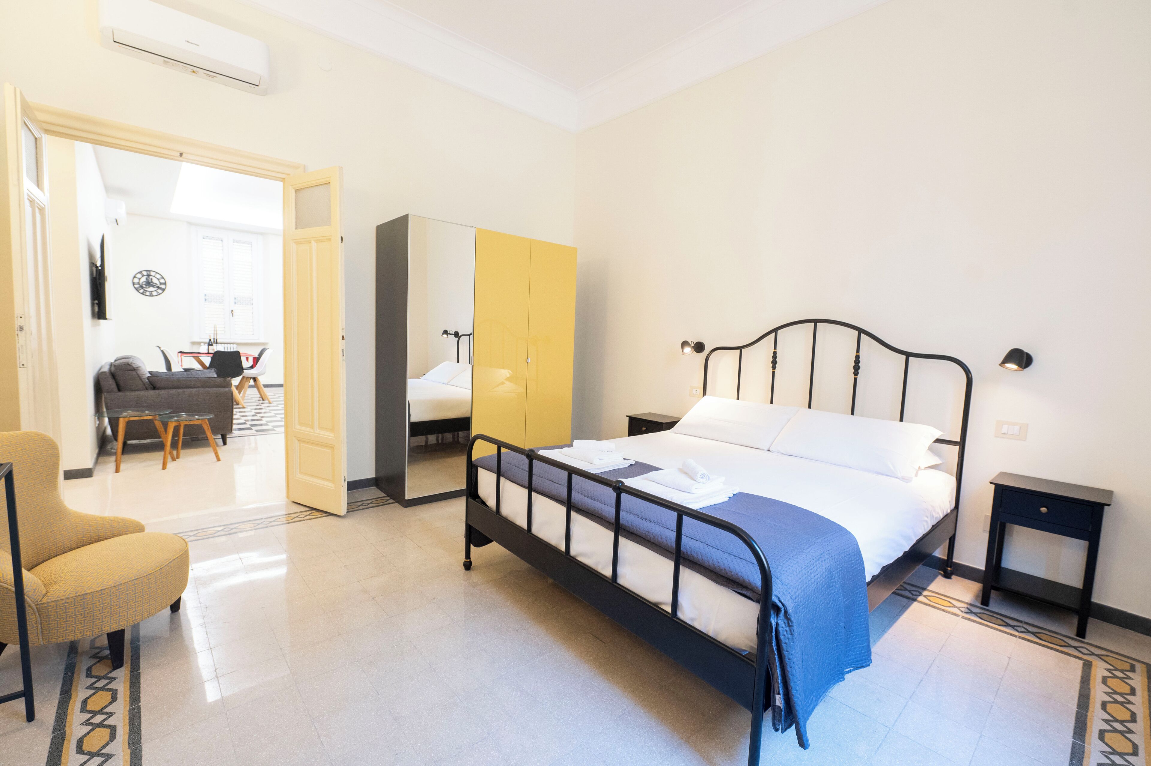Quarto de hotel com cama, cadeira, guarda-roupa e uma mesinha.