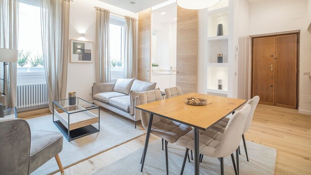 A modern living room with a sofa, a glass coffee table, a dining table with chairs, and a wooden door.