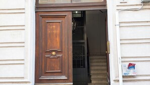 A wooden door with a brass handle and a metal latch, leading to a staircase inside a building with a white exterior and a small sign on the wall.