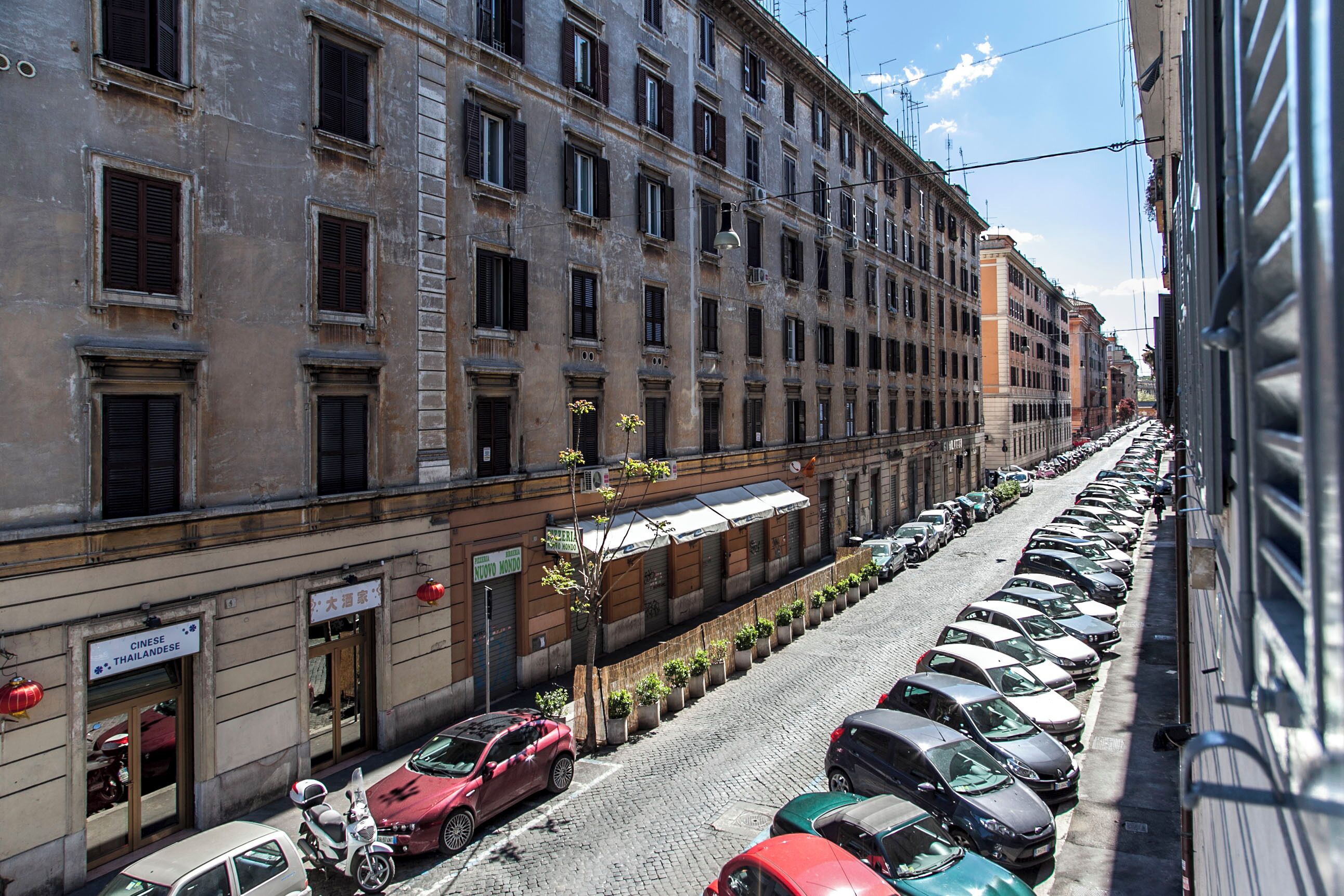A row of parked cars along a cobblestone street adjacent to a multi-story building with signs indicating Chinese and Thai restaurants.