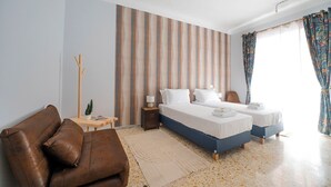 Ett hotellrum med två sängar, en brun lädersoffa, ett litet träbord med en lampa och en randig vägg.