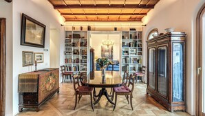 A dining area with a round table, chairs, a chandelier, bookshelves, and a cabinet. - Trastevere Outstanding 4 Br Terraced Apartment (Rome)