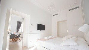 A modern bedroom with a large bed, a flat-screen TV, and a dining area visible through an open door. - Vatican Beautiful 2Br Apartment  (Rome)