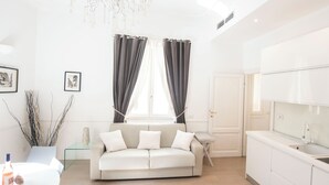 A modern living room with a sofa, a glass coffee table, and a dining table. There is a kitchen area with a sink and cabinets. - Vatican Beautiful 2Br Apartment  (Rome)