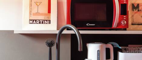 Una cocina con un lavamanos negro, un microondas rojo, una cafetera blanca y un cuadro con un anuncio de Martini.